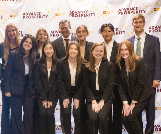 A group of students in business professional clothing msiling with a male faculty member.