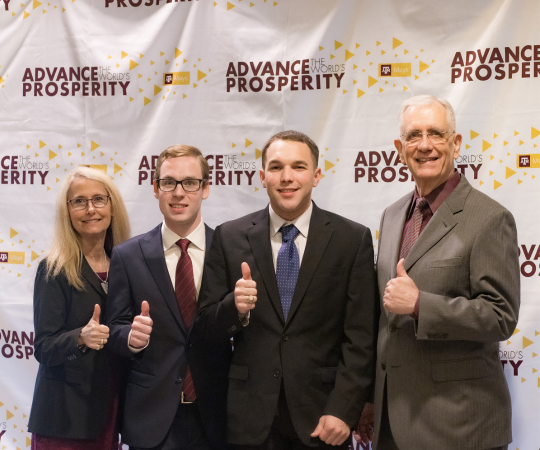 A group of people smiling in business professional clothing and giving a thumbs up.