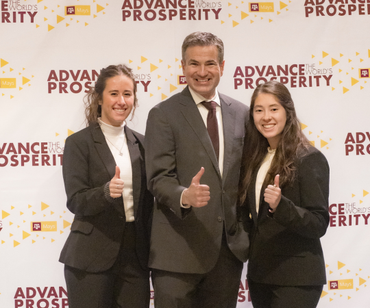 Two female students smiling and giving a thumbs up alongside an accounting faculty member.