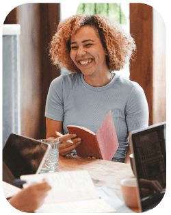A student smiling at a table while holding a book.