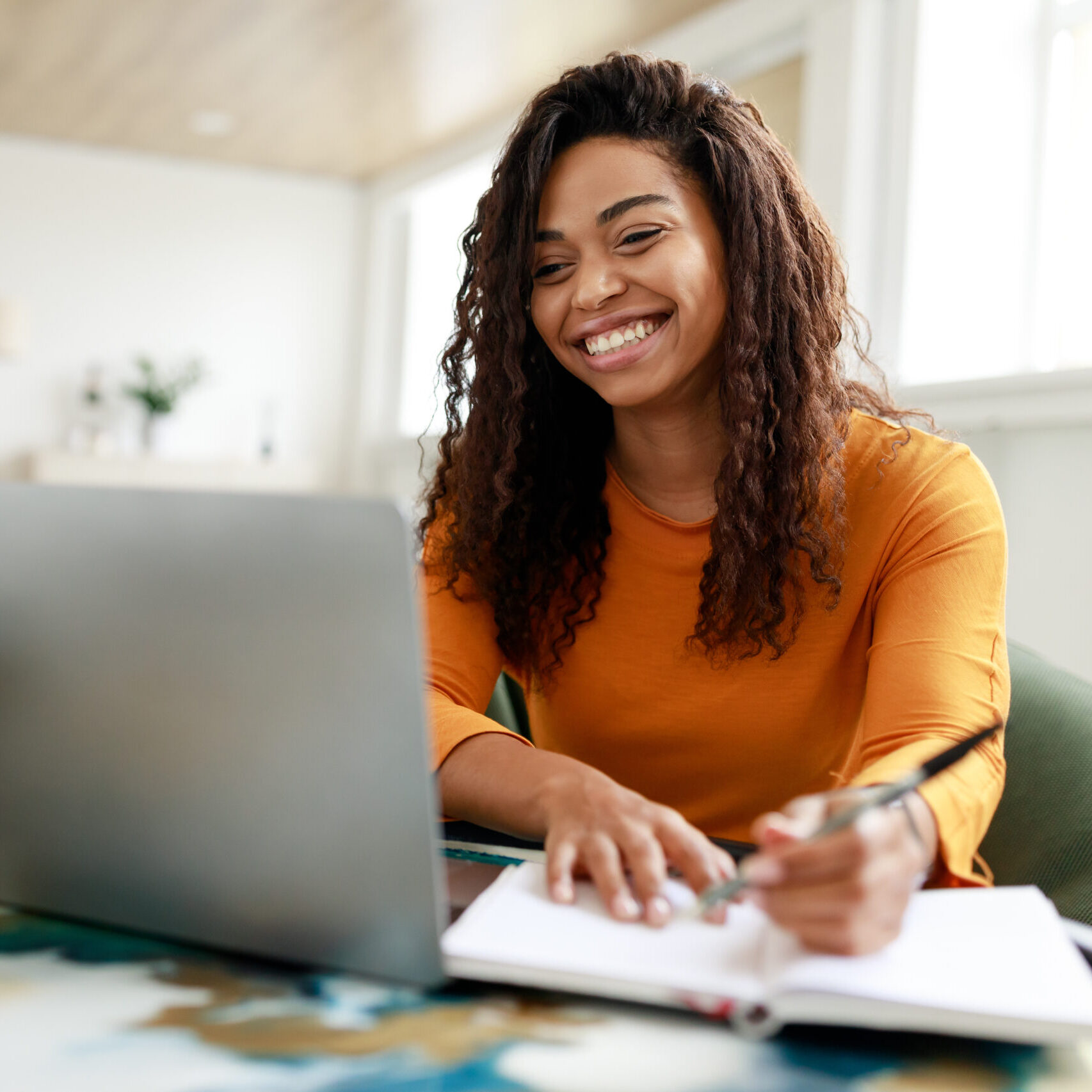 Woman sitting at desk, using computer and writing in notebook