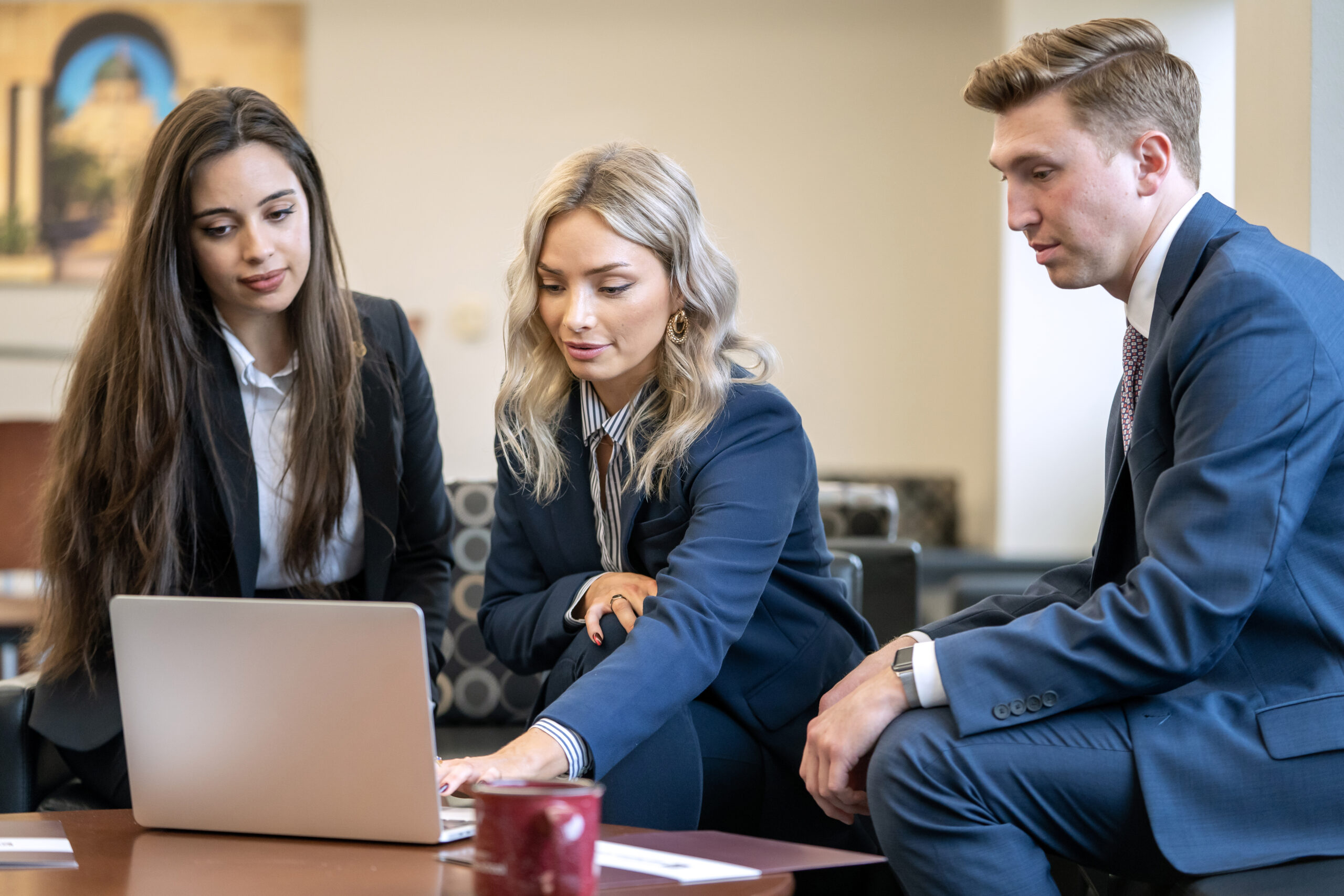 Three students in business formal looking at a laptop screen