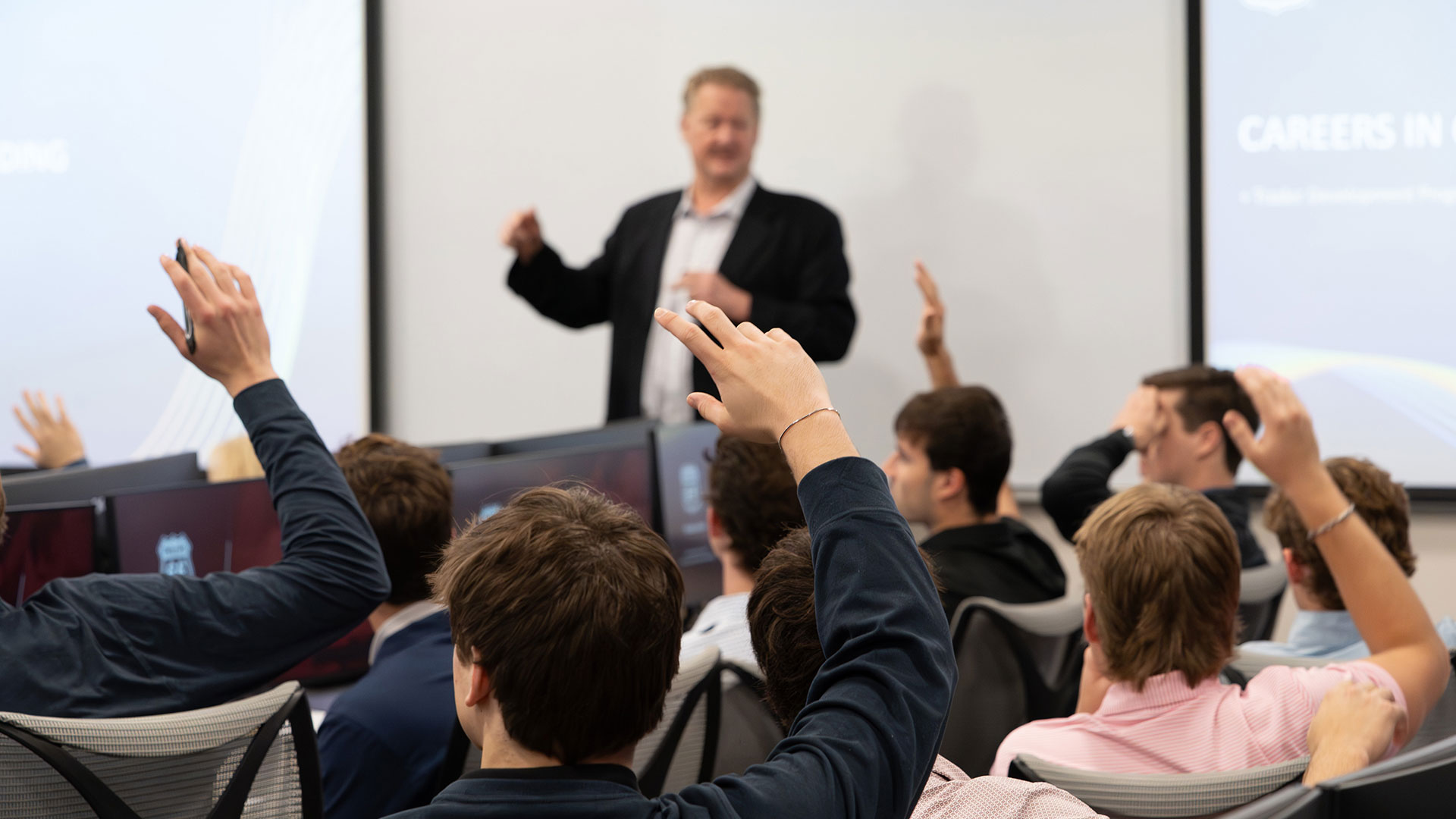 Students raising their hands to answer in a trading class